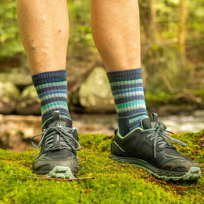 Close up lifestyle shot of model wearing Decade stripe hiking socks in Denim, standing on moss in the woods.