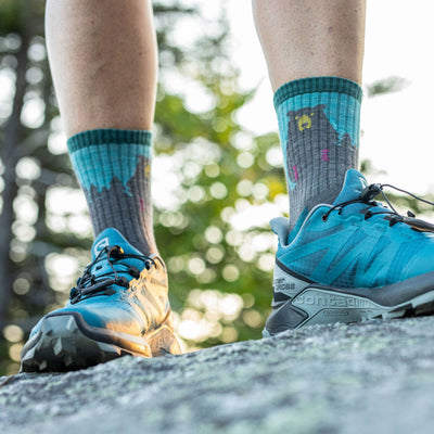 Close up of model standing on a rock, wearing bear town socks in aqua and trailrunners.
