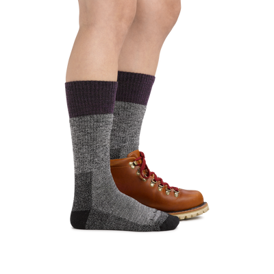 Profile image of a woman's legs on a white background, facing right, wearing Women's Scout Boot Midweight Hiking Socks in Plum with one foot in a hiking boot