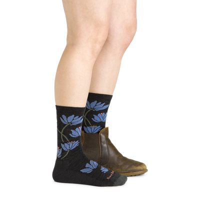 Side studio shot of model wearing women's lillies crew lightweight lifestyle sock in charcoal with brown boot on left foot