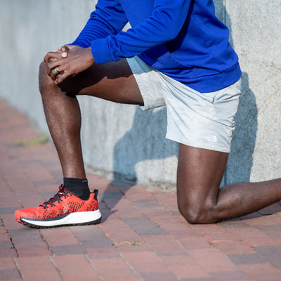 Side shot of a model kneeling on a brick pathway wearing the men&