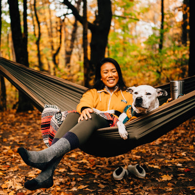 Lifestyle shot of woman smiling with her dog in her hammock. It is fall in Vermont and she&