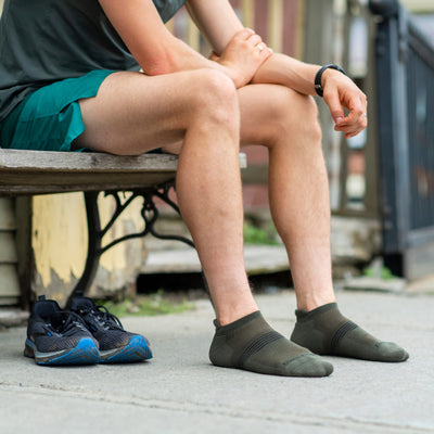 Runner seated on bench about to put on workout shoes over his men's athletic no show socks in fatigue green