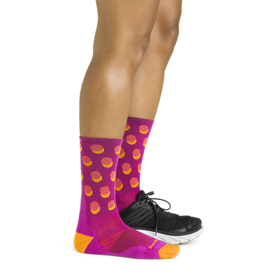 Side shot of model wearing the women's circuit micro crew running socks in clover pink with a black sneaker on her left foot