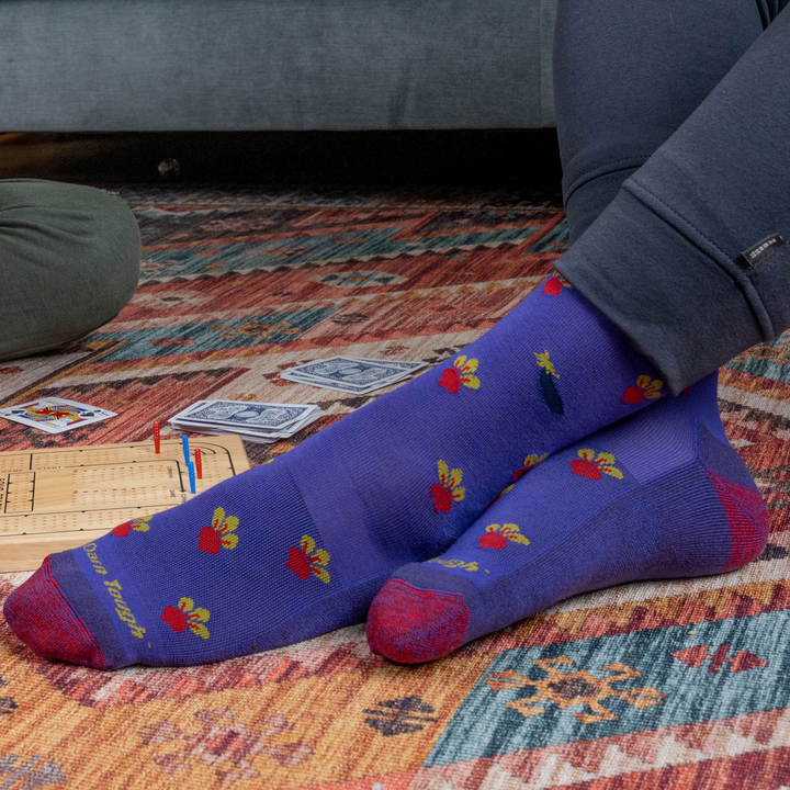 Close up shot of model sitting on the floor playing cards wearing the men's beets crew lifestyle sock in eggplant