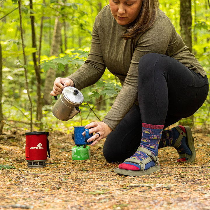 Side shot of model pouring hot water at their campsite wearing the women's ray day micro crew hiking socks in denim blue
