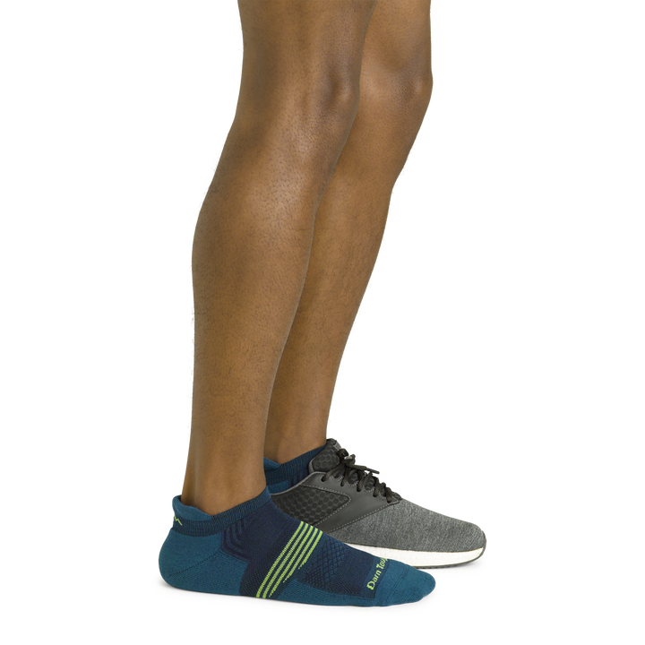 Side shot of model wearing the men's element no show tab athletic sock in dark teal with a gray sneaker on his left foot