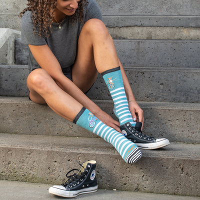 Woman seated on steps pulling on converse over the Animal Haus lifestyle socks in blue with a unicycling lemur