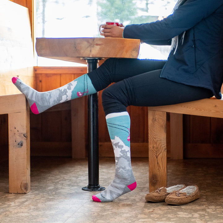 lifestyle shot of model wearing yeti ski socks, sitting at cafe table drinking coffee before going out skiing.