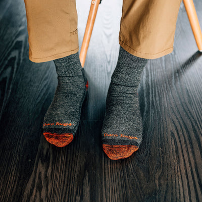 Close up overhead shot of model wearing men's nomad boo hiking sock in pewter gray with dark wood floor in the background