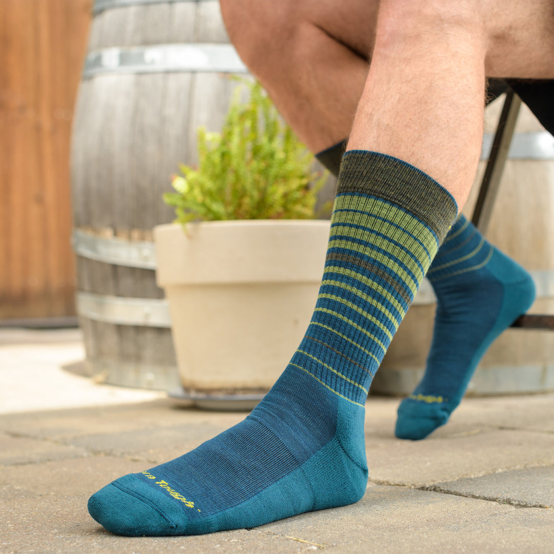 Close up shot of model sitting in a chair outside wearing the men's frequency crew lifestyle sock in dark teal