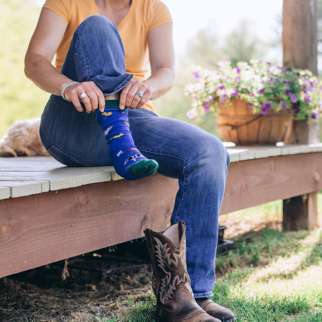Full shot of model sitting on a wood bench outside putting on the barnyard VT Foodbank crew lifestyle sock