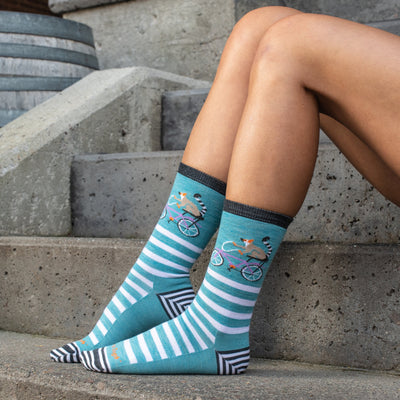 Women's feet on stairs showing off the casual Animal's Haus socks in aqua with a biking lemur