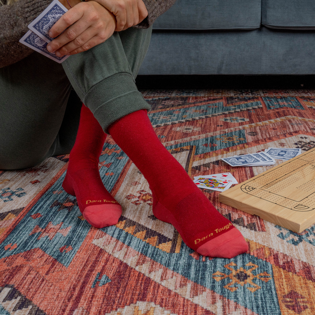 Close up shot of model sitting on a couch wearing the women's basic crew lifestyle sock in cranberry while playing cards