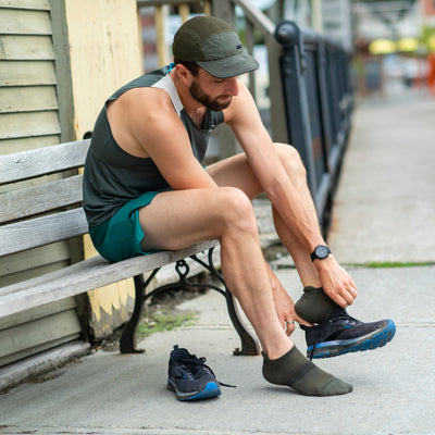 Athlete seated on bench pulling on workout shoes over the Element no show socks in fatigue green