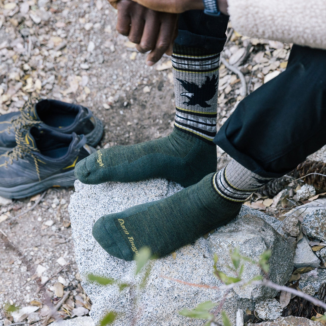 Close up shot of model sitting on a rock outside while wearing men's vangrizzle boot hiking sock in forest green